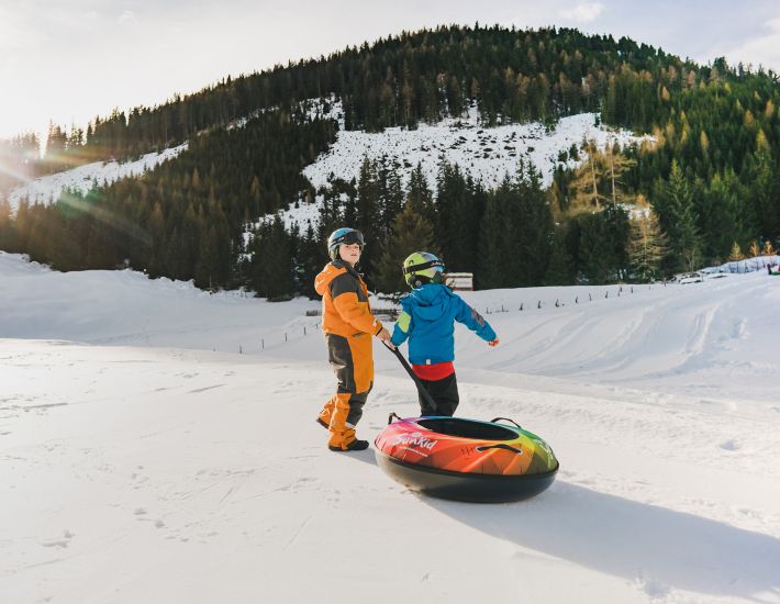 Ein Erwachsener und ein Kind ziehen einen bunten Snowtubing-Schlitten im Schnee bei Innerkrems