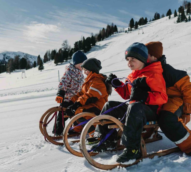 Vier Kinder sitzen auf Holzschlitten und genießen das Schlittenfahren im Schnee bei Schönfeld