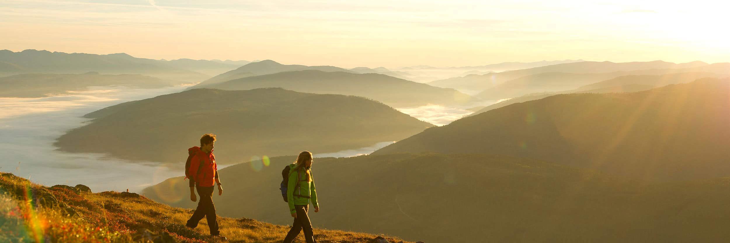 Zwei Wanderer genießen den Sonnenaufgang über einer nebelverhangenen Berglandschaft bei einer Herbstwanderung in Katschberg