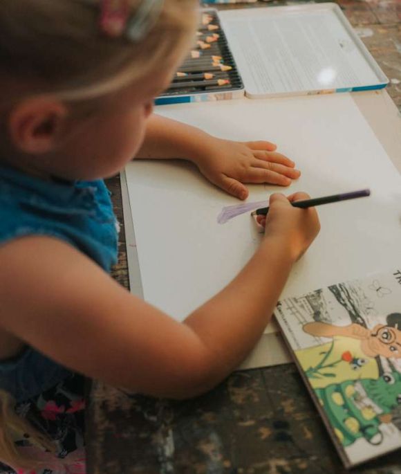 Ein kleines Mädchen malt mit Farbstiften auf einem Blatt Papier bei einem Kindermalkurs