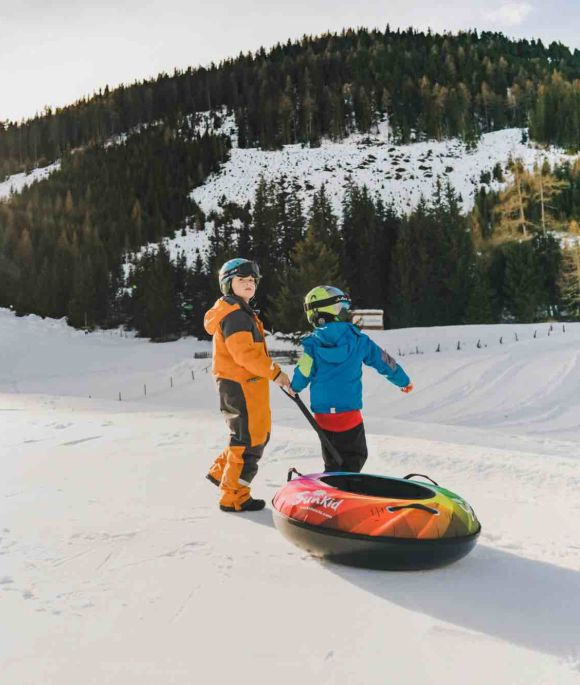 Ein Erwachsener und ein Kind ziehen einen bunten Snowtubing-Schlitten im Schnee bei Innerkrems